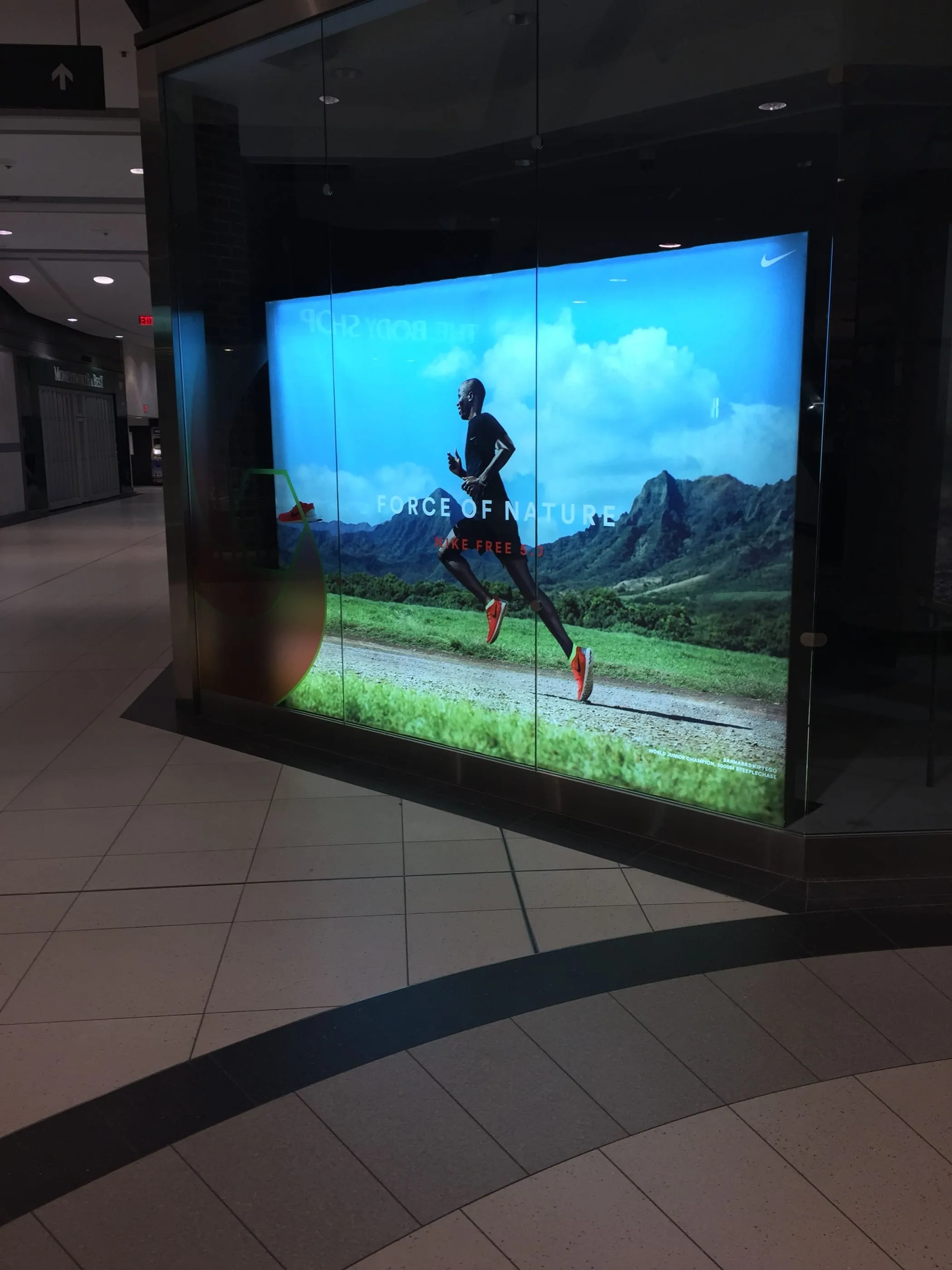 Large backlit lightbox graphic of a runner in a mall corridor